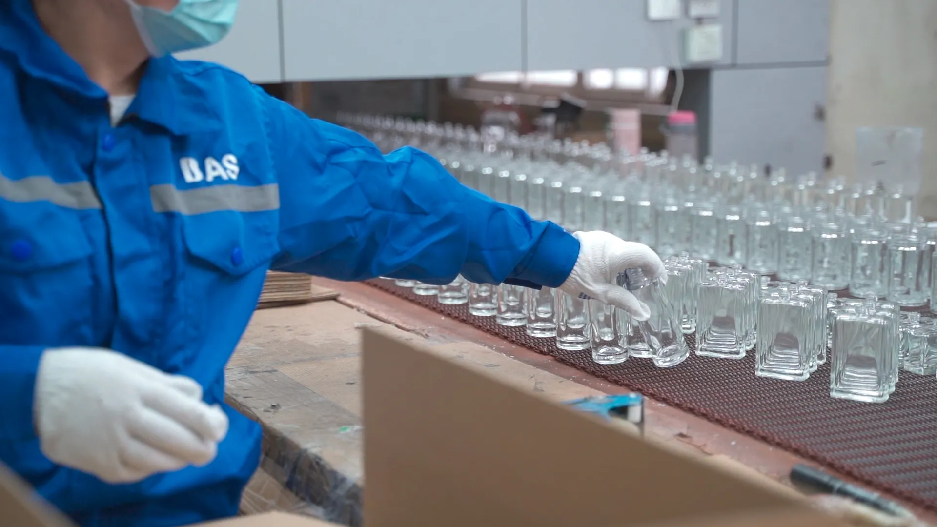 Quality technician manually inspecting clear glass containers after automated inspection